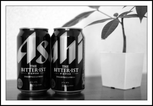 A black and white 3:2 ratio landscape orientated photograph of two cans of Asahi The Bitter-ist beer and a potted baby Ficus benjamina. The two black beer cans take up most of the left half of the photograph. Benjamin sits on the right side a little behind the cans but separate from them. The cans are lined up so that the left can shows the large first two golden letters of Asahi whilst the right can displays the remaining three letters. The tip of one of Benjamin’s leaves looks as if it touches the top of the can (again that flat fun from photography). The angle the leaf makes (sloping down around 30 degrees from the horizontal) matches (almost) the slope of the top of the letters ‘a’ and ‘h’ of the second can. Quite pleasing. I didn’t notice the touch potential when I set up nor again when taking the shot. I must learn from that. Slow down when shooting objects/subjects that are not going to move. Earlier today I returned to take an identical shot to one I took a few weeks back. I was editing that older shot in Picture Window Pro last night and noticed that a couple of tweaks would make the composition a little stronger. The shot was taken nearby and the cooler temperatures we have today meant I could do a slightly longer walk to my local supermarket. So set up the repeat shot I did. Walking away, I decided to check that all was aligned only to notice that two elements were now distractingly overlapping. So third time a charm, right? Well almost. Checking the shots back home what I wanted to align was aligned, but it is just a tad off. I must go back a fourth time. Message to self: measure twice cut once but translated to photography workflow. Back to beer. This Asahi beer is a new release for the summer. It’s not best bitter as I know it from the UK but it’s close. Asahi is not a brand I typically drink. My Japanese beer brewer of choice is Sapporo and their Ebisu brew. How about you, dear reader, what is your beer tipple of choice?